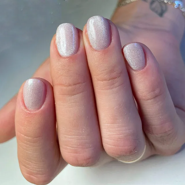 Hånd med korte, runde negler lakkert i skimrende perlehvit farge.