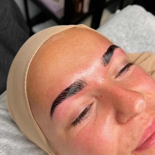 Kvinne med kraftig markerte bryn og nøytral sminke, smiler etter behandling.